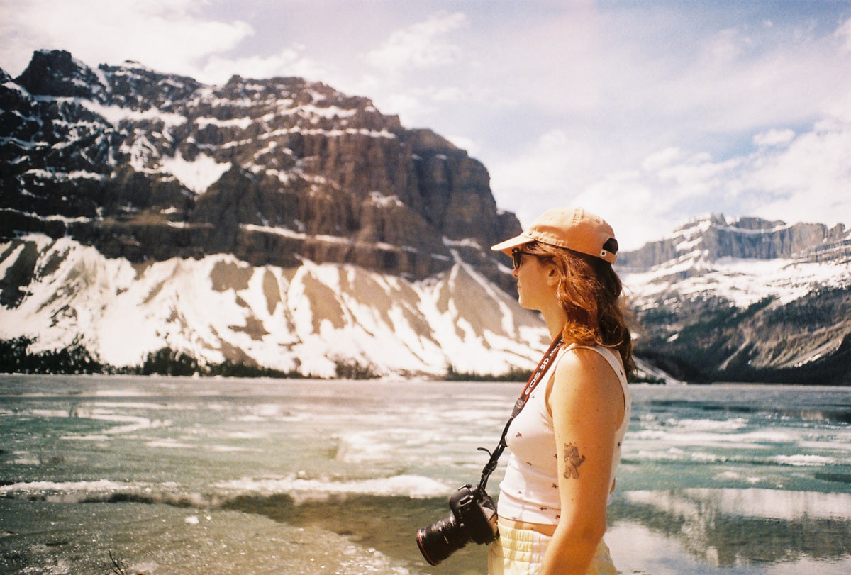 La photographe au bord d'un lac gelé des Rocheuses, appareil argentique autour du cou