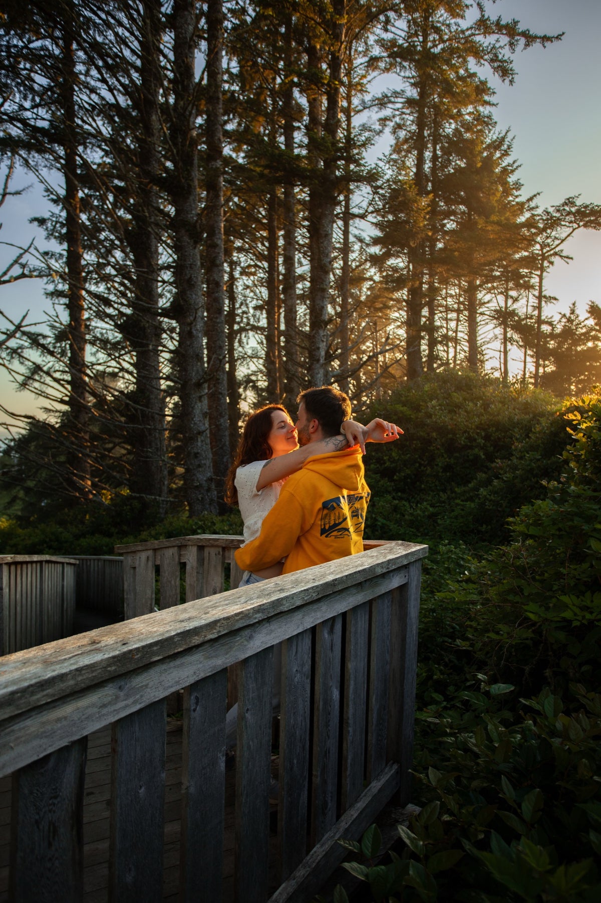 Le couple enlacé sur une passerelle en bois, au coucher du soleil dans une forêt de pins